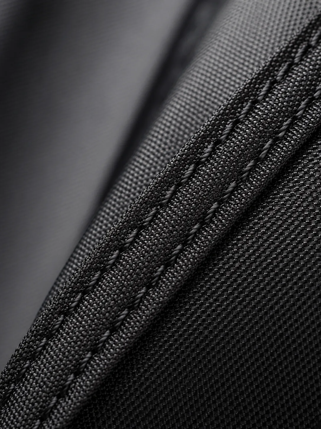 Macro close-up of the bag's black woven fabric with a webbing strip held down by a double row of stitching