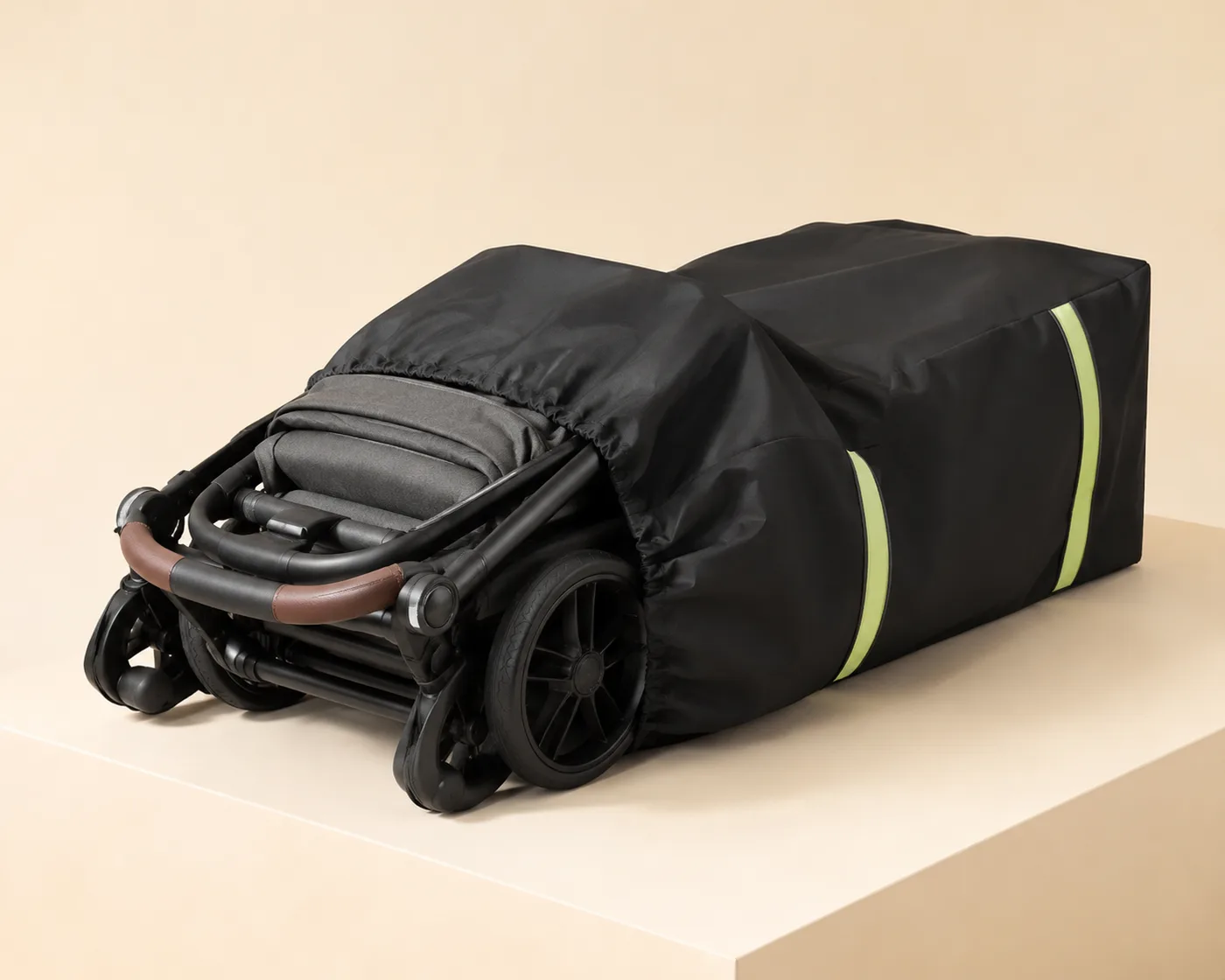 Black stroller travel bag with two green reflective stripes pulled halfway over a folded stroller resting on a beige studio block
